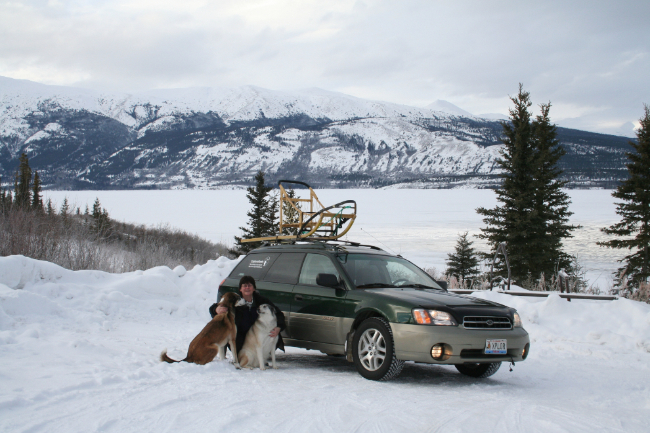 Cathy with our huskies, dog sled, and Subaru Outback at our Carcross vcabin
