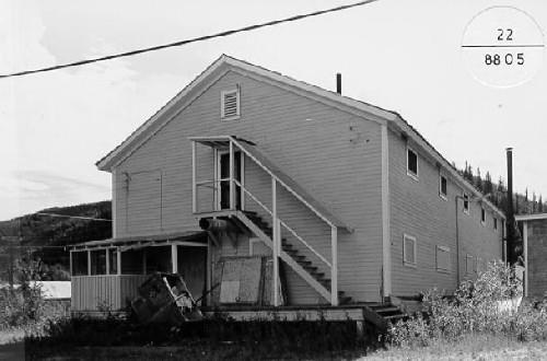 Corner view of the Mess Hall and Bunkhouse, showing the arrangement and detailing of its doors and windows, its porches, and its covered stair, 1988. Photo by Parks Canada.