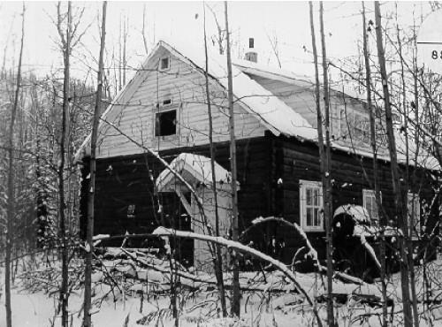 View of the main entrance to the Troberg Residence at Bear Creek, showing its exposed saddle-notched log walls, its horizontal siding above the roof line, and its gable roof, 1988. Photo by Parks Canada.