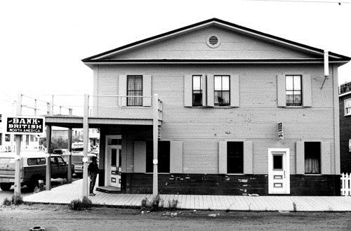 Facade of the Bank of British North America, showing the pedimented gable roof, the circular ventilator piercing the pediment, and the overhanging eaves, 1988. Photo by J. Mattie, via Parks Canada.