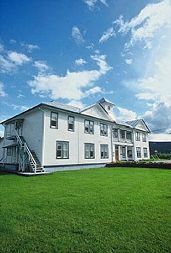 Corner view of the Former Territorial Court House emphasizing the monumental presence and dominant profile of the building with its long, rectangular two-and-a-half-storey massing under a metal hipped roof topped with a lantern, 1995. Photo by W. Lynch, via Parks Canada.