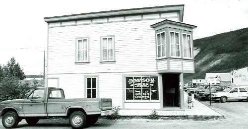 View of the main entrance to Harrington's Store in Dawson, showing the square-sided oriel window placed at the salient angle, the richly ornamented double front door, and the painted cove siding, 1987. Photo by Department of the Environment.
