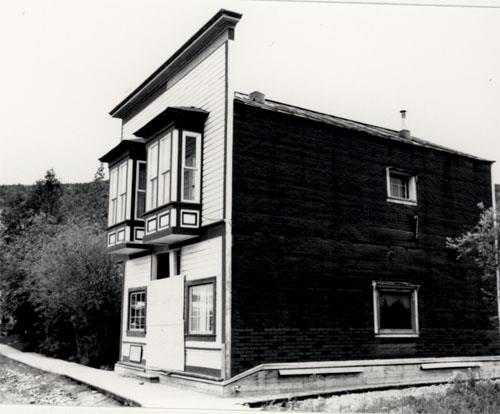 General view of Ruby's Place, showing the horizontal, painted, coved siding of the street facade with its distinctive, large oriel windows, 1987. Photo by Parks Canada.