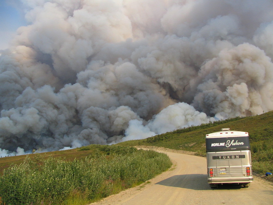 A Norline Coaches MCI tour bus stopped on the Taylor Highway by a wildfire.