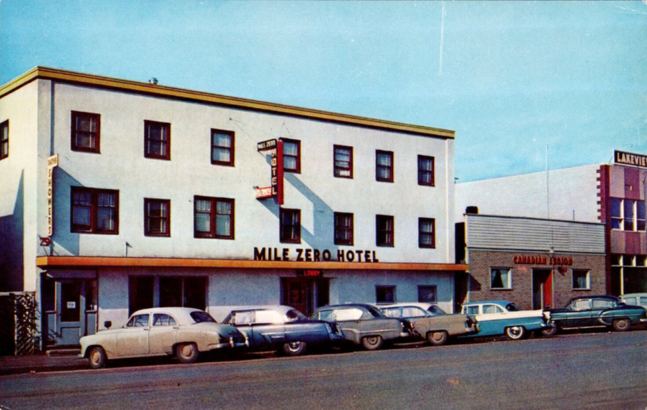 Postcard showing the Mile Zero Hotel with several vehicles in front, in about 1960.