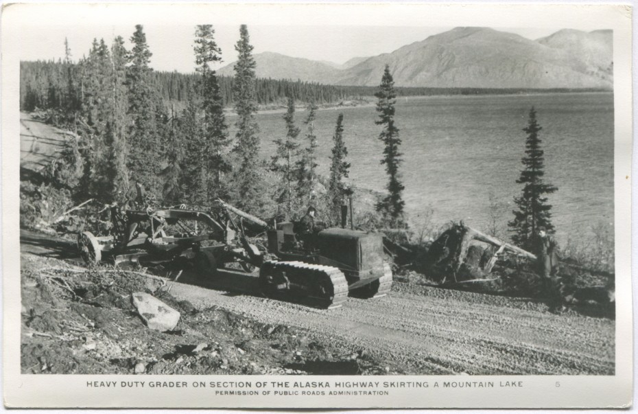 Postcard showing a Cat pulling a grader on a new section of the Alaska Highway along Kluane Lake, Yukon